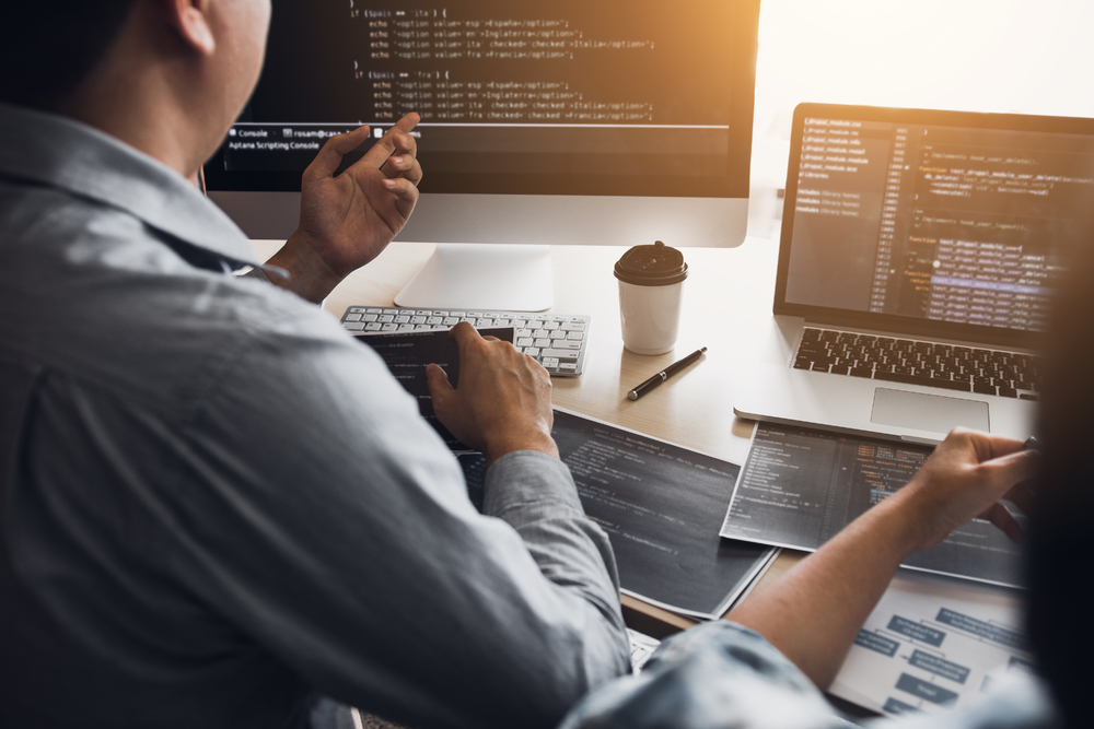 兩名軟件開發(fā)人員正在使用計(jì)算機(jī)與辦公桌上的合作伙伴一起工作